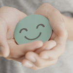 A person holding a smiley face sticker with their hands cupped facing out.